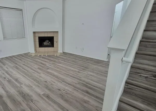 a view of an empty room with wooden floor and a fireplace
