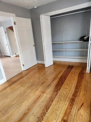 a view of an empty room with wooden floor and closet