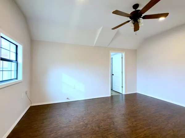 an empty room with wooden floor fan and windows