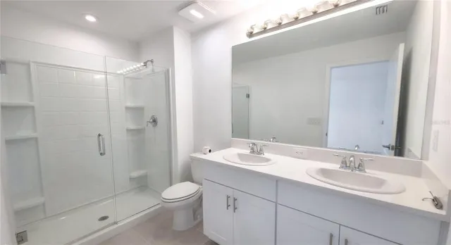 a bathroom with a double vanity sink toilet mirror and shower