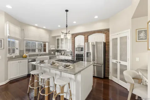 a kitchen with stainless steel appliances kitchen island granite countertop a refrigerator a oven a sink and white cabinets with wooden floor