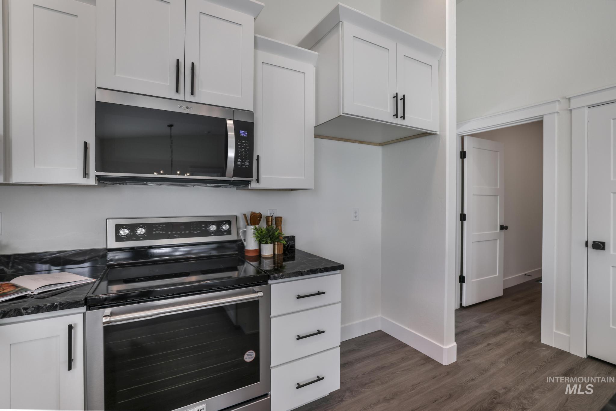 921 Adamite Road Kimberly, ID 83341 - Photo 11 of 25 Kitchen featuring stainless steel appliances, white cabinetry, dark wood-style flooring, and dark stone counters