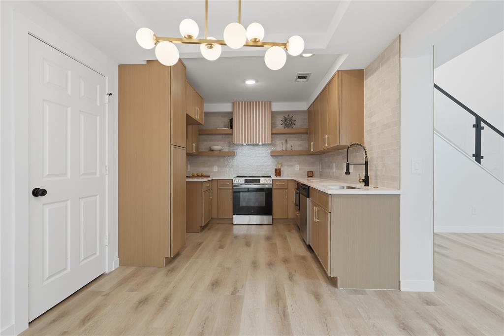 17118 Planters Row Addison, TX 75001 - Photo 7 of 18 Modern kitchen featuring light wood-finish cabinetry, stainless steel appliances, a matte black faucet, and a contemporary chandelier