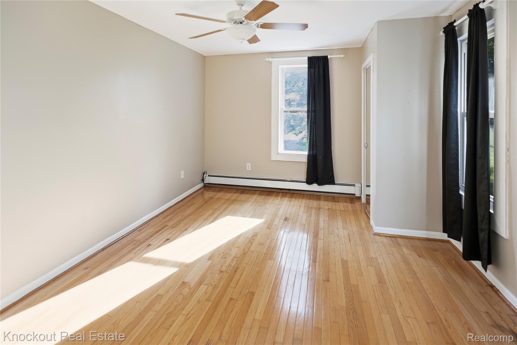 5750 Maple Road Frankenmuth, MI 48734 - Photo 20 of 60 Hardwood flooring, two windows with black drapery, ceiling fan, neutral wall tones, and white trim
