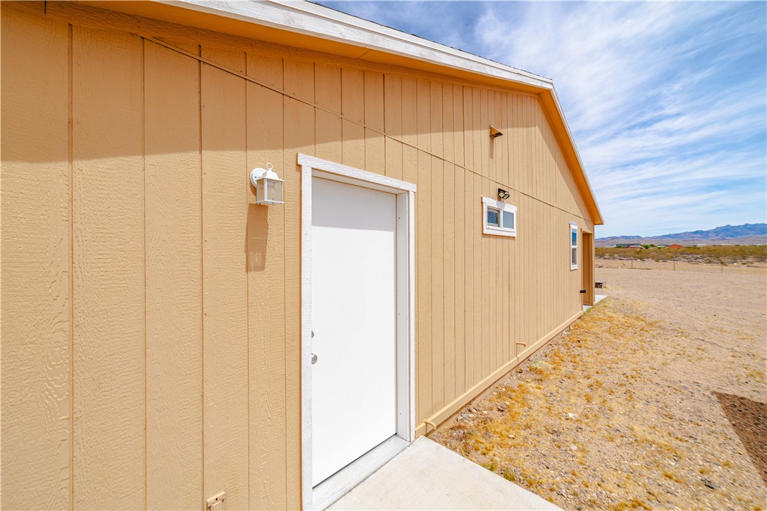 2948 Pinal Road Golden Valley, AZ 86413 - Photo 33 of 59 Light-toned siding exterior with vertical panels, a white entry door, and a white outdoor lantern fixture