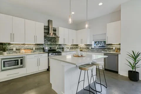 a kitchen with kitchen island granite countertop a sink a stove a refrigerator and white cabinets with wooden floor
