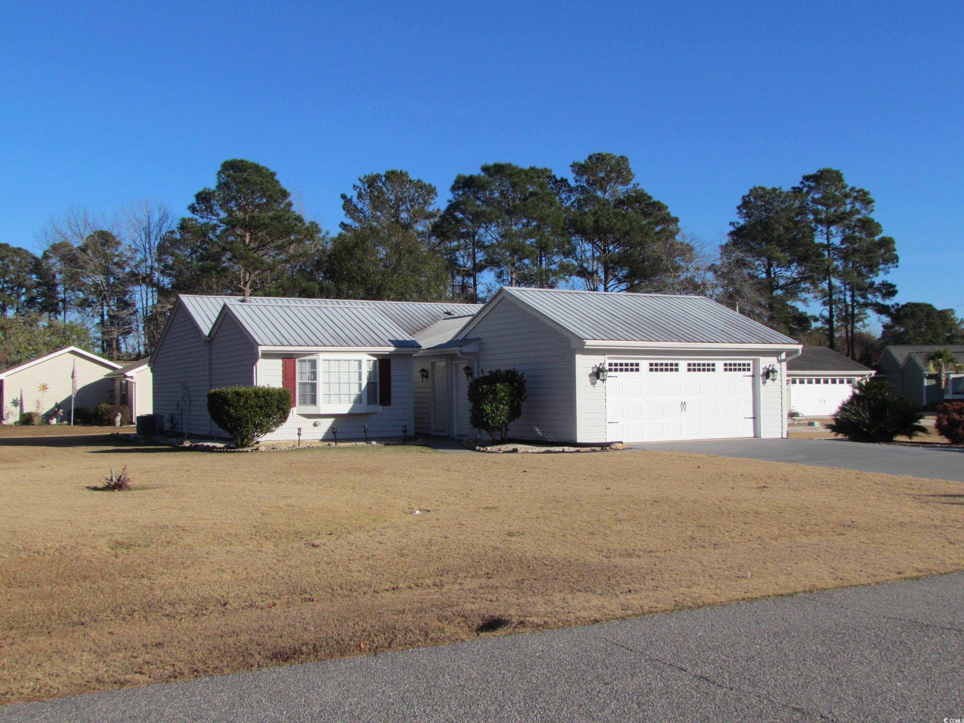 Ranch-style house featuring a front yard, a metal roof, and driveway