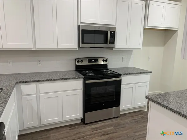 a kitchen with stainless steel appliances granite countertop a stove a microwave and a white cabinets