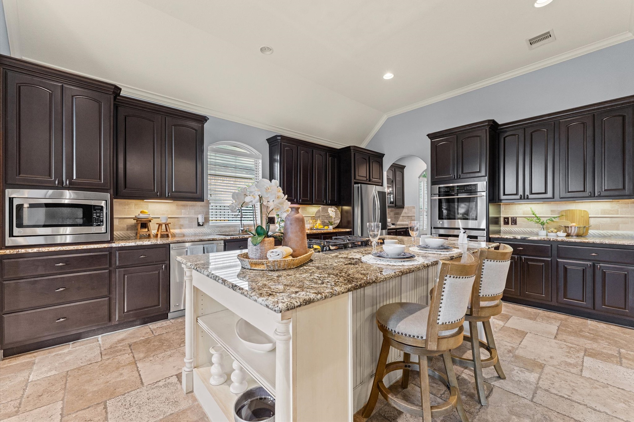70 Valera Ridge Drive Spring, TX 77389 - Photo 15 of 37 This spacious kitchen features dark wood cabinets, granite countertops, and a central island with seating. Stainless steel appliances and a tiled floor complete the elegant look, offering a perfect blend of style and functionality for cooking and entertaining.