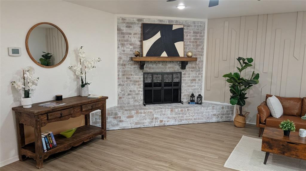 1205 Augusta Road Benbrook, TX 76126 - Photo 12 of 21 Whitewashed brick fireplace with a wood mantle and dark metal screen, complemented by plank-style flooring