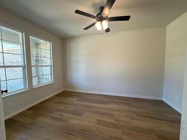 an empty room with wooden floor fan and windows