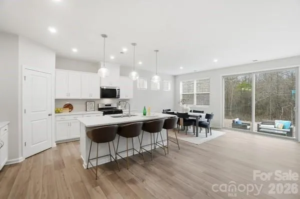 a kitchen with stainless steel appliances a stove a refrigerator a kitchen island a sink cabinets and chairs with wooden floor