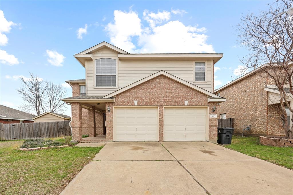 Traditional-style home with brick siding, an attached garage, driveway, and fence