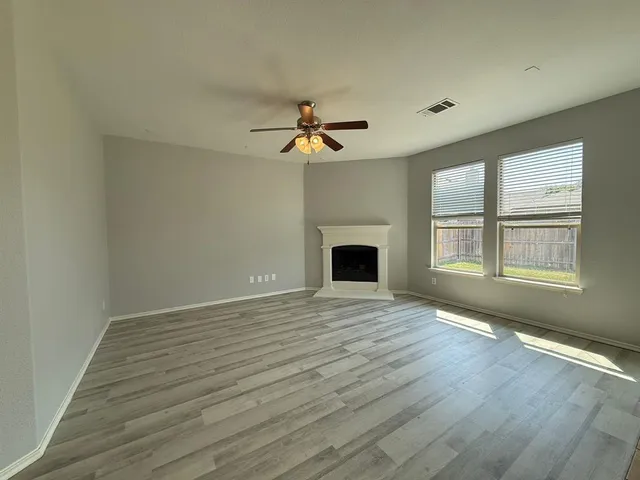 an empty room with wooden floor fireplace and windows