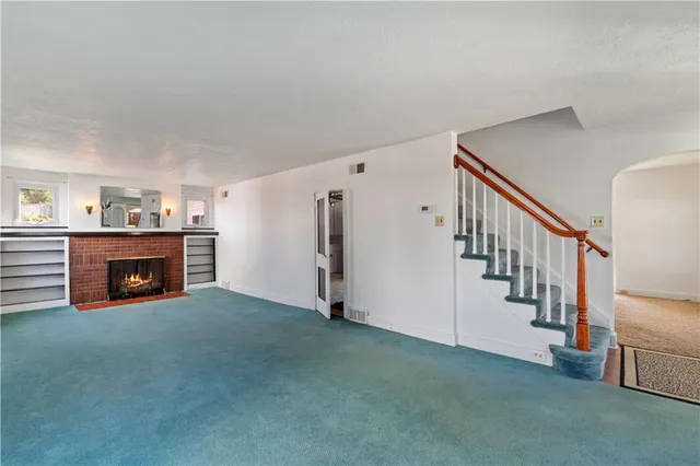 a view of an empty room with fireplace stairs and a way to room with wooden floor