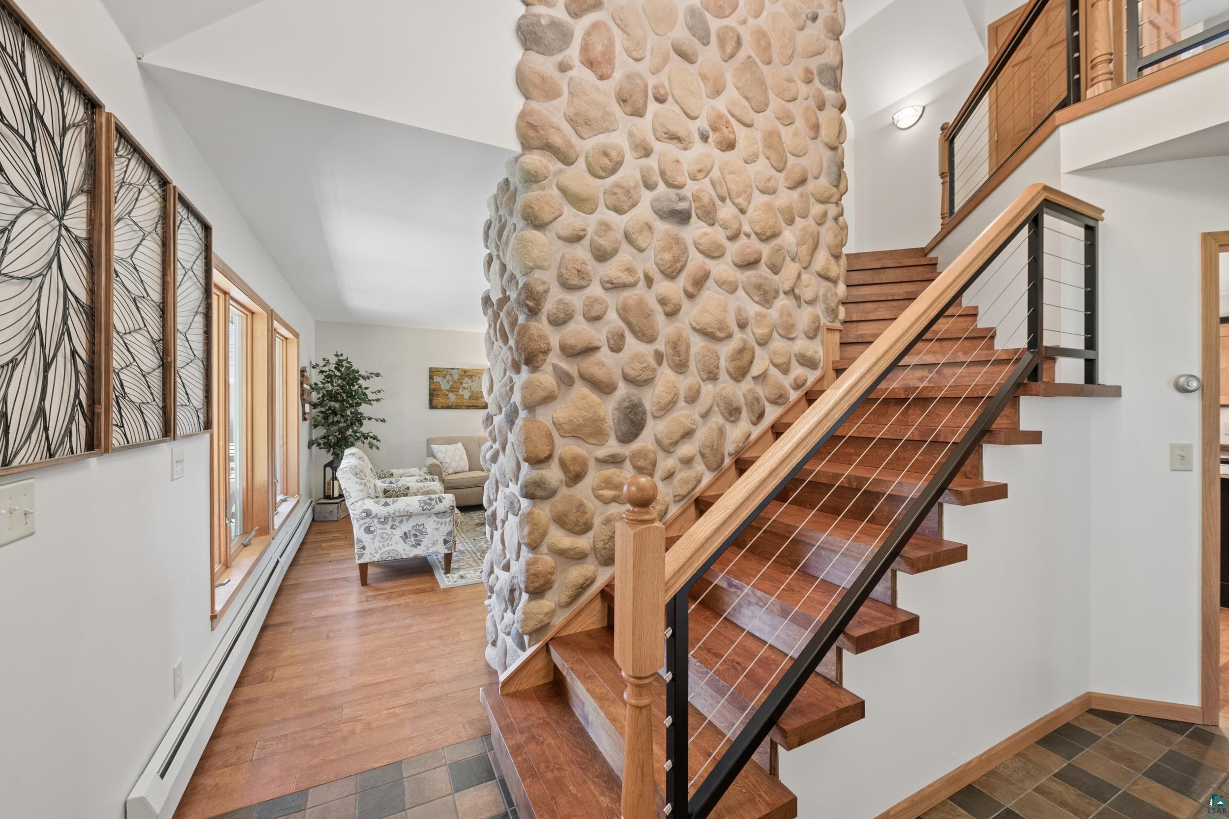 3113 Golf Course Road Ashland, WI 54806 - Photo 14 of 38 Foyer featuring a prominent stone accent wall, natural wood staircase with cable railing, wood-finish flooring, and multiple large windows