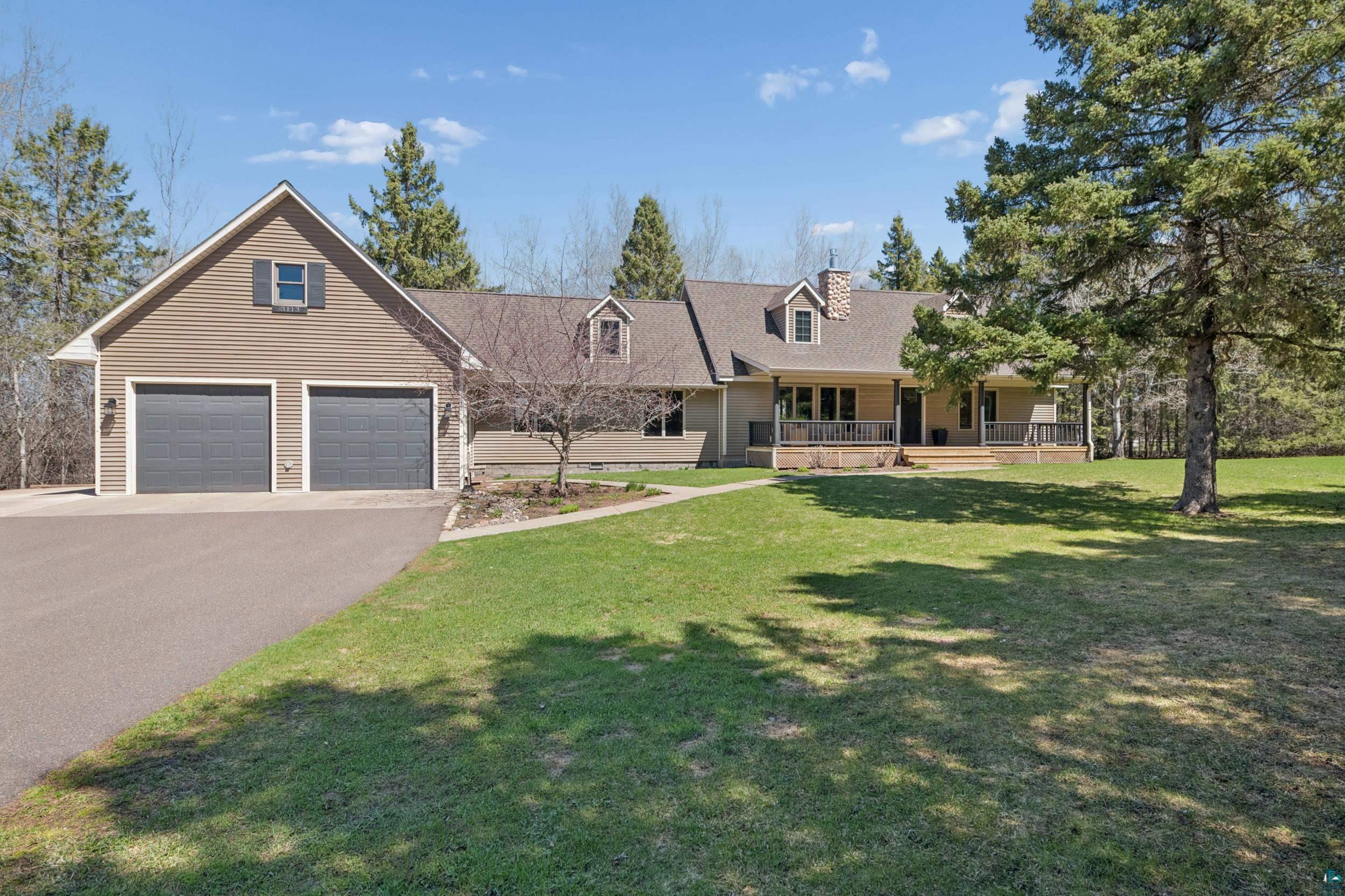 3113 Golf Course Road Ashland, WI 54806 - Photo 2 of 38 Ranch-style residence featuring a two-car attached garage, dormer windows, a covered front porch, and a stone chimney accent