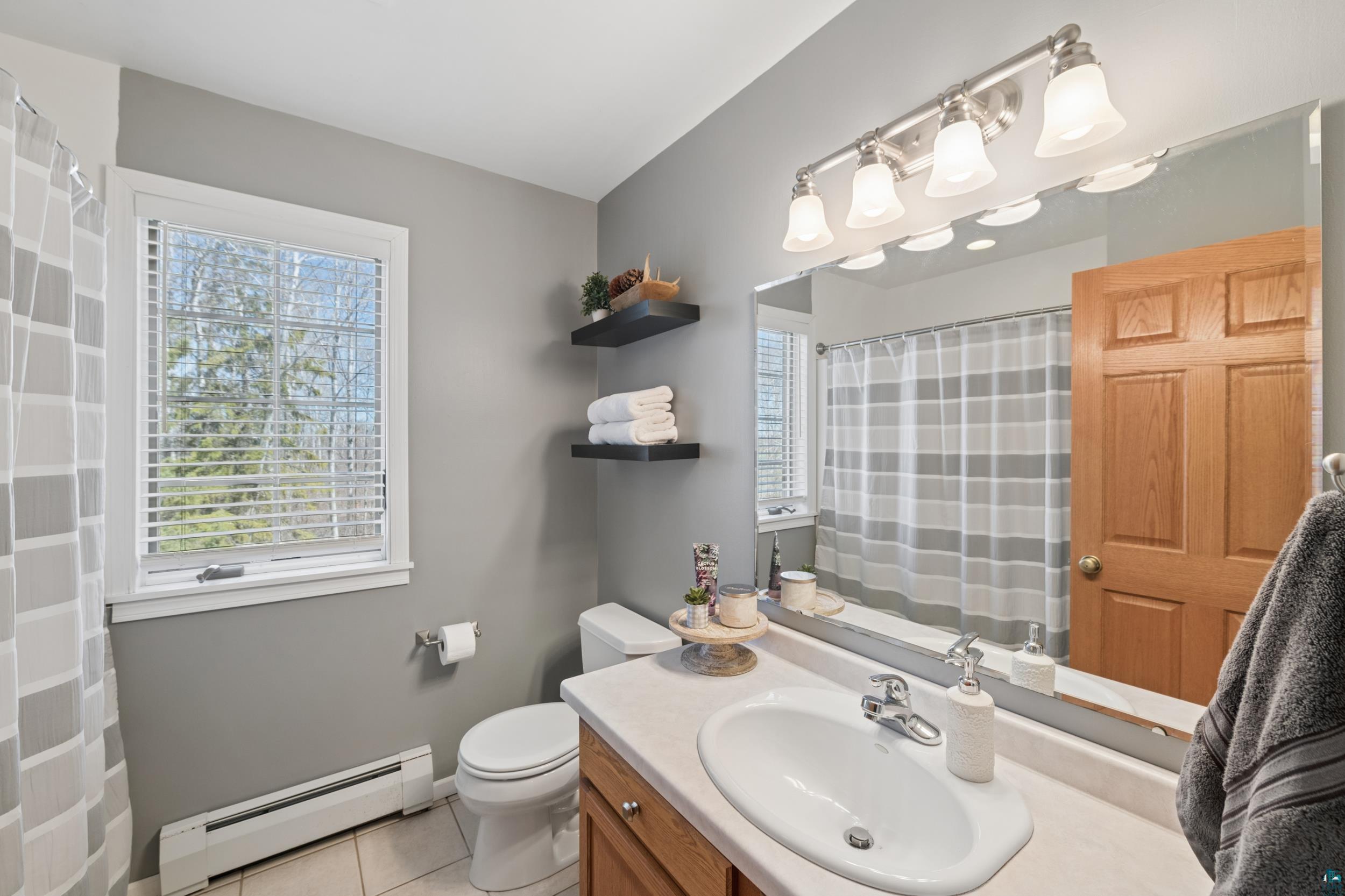 3113 Golf Course Road Ashland, WI 54806 - Photo 25 of 38 Full bathroom featuring a wood-finish vanity with an integrated sink, a large wall-mounted mirror, and a window with blinds