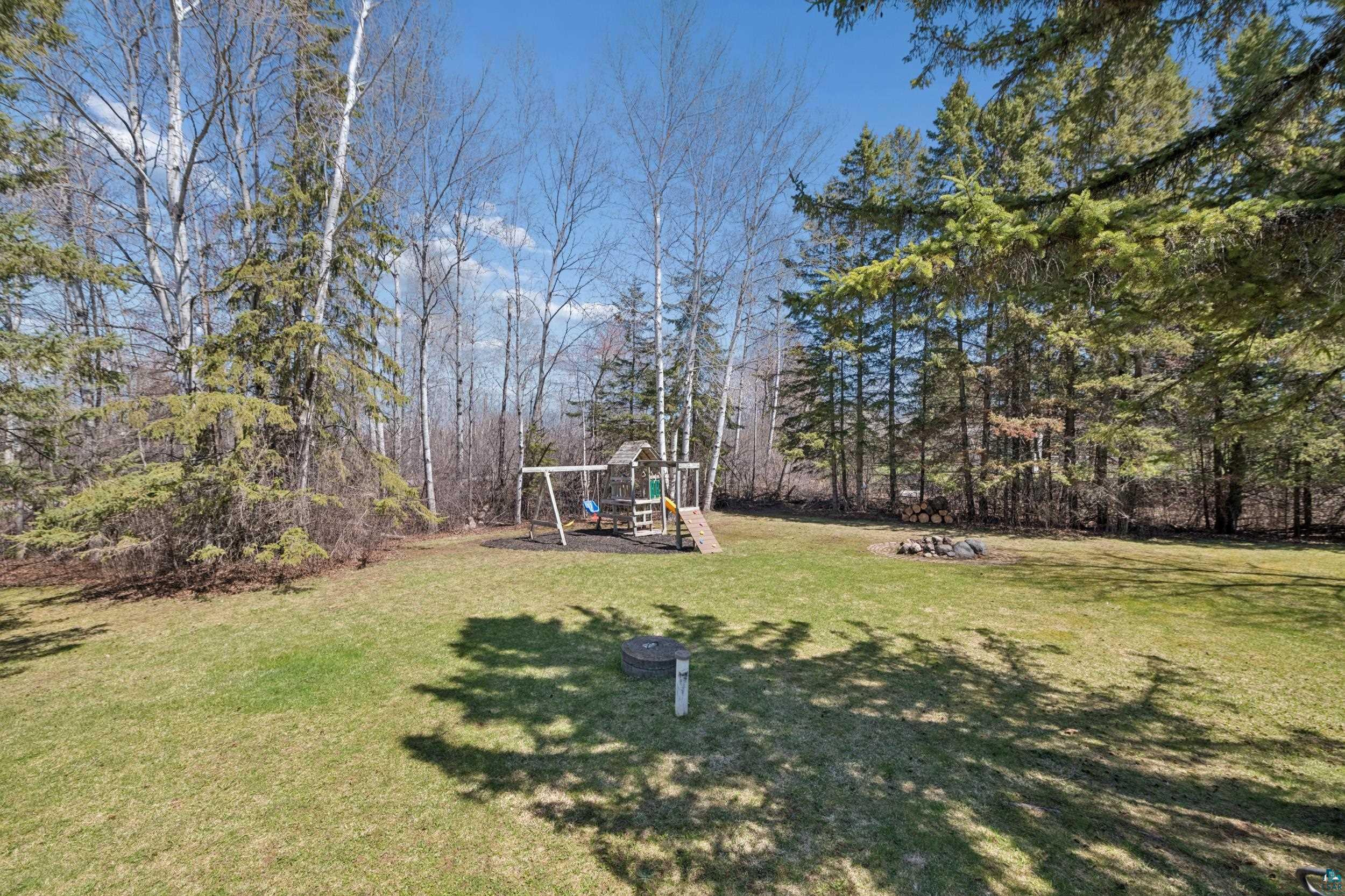 3113 Golf Course Road Ashland, WI 54806 - Photo 34 of 38 Expansive green lawn surrounded by mature trees, featuring a dedicated play structure with swings and a slide, and a defined fire pit area
