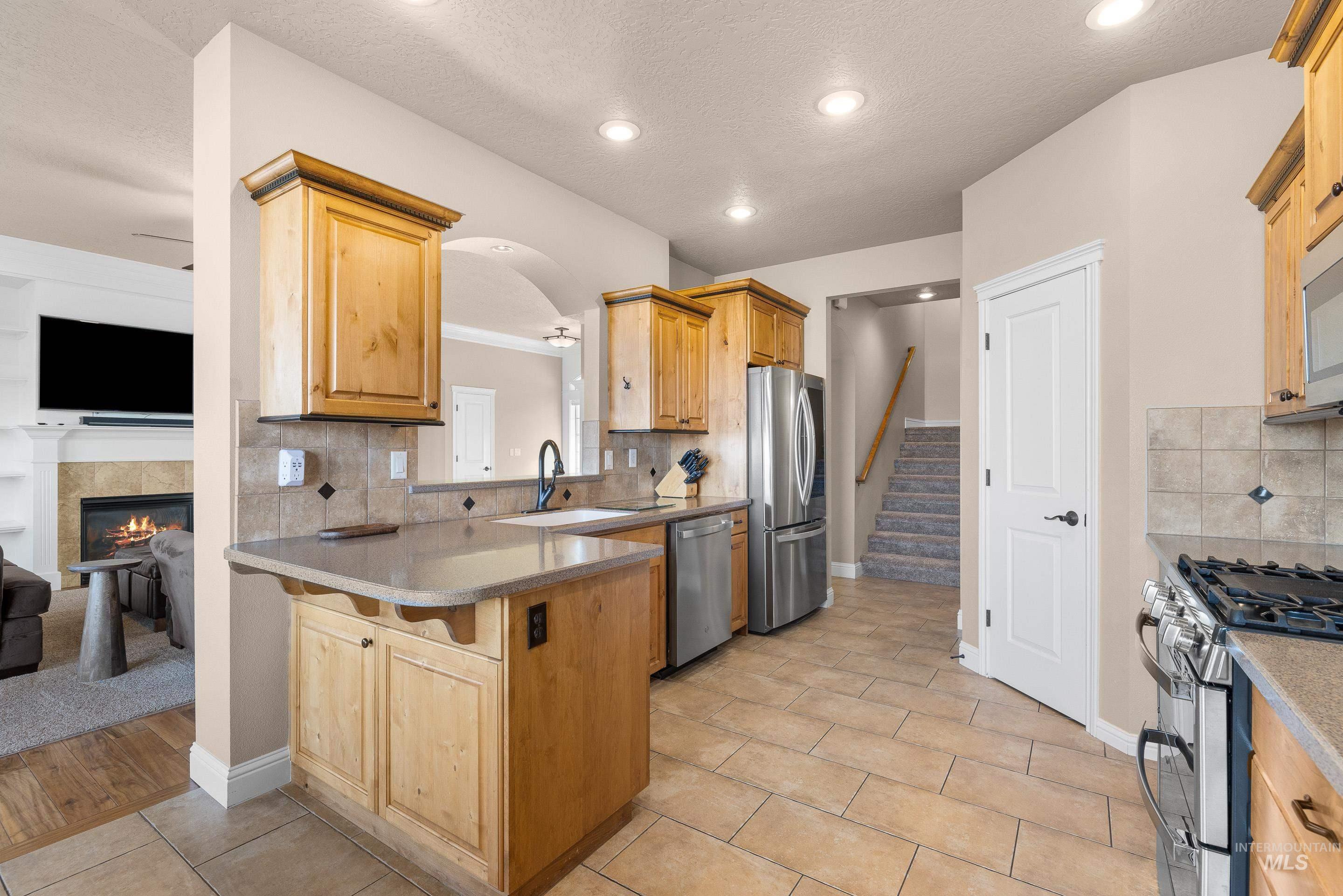 2208 East Sicily Street Meridian, ID 83642 - Photo 16 of 50 Kitchen featuring decorative backsplash, appliances with stainless steel finishes, a tile fireplace, arched walkways, and light tile patterned floors