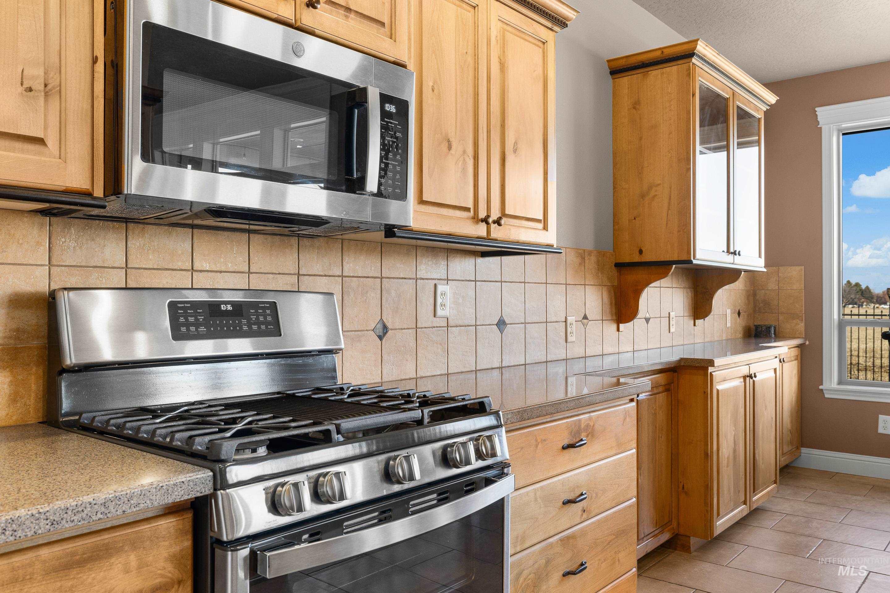 2208 East Sicily Street Meridian, ID 83642 - Photo 19 of 50 Kitchen with appliances with stainless steel finishes, backsplash, glass insert cabinets, and light tile patterned floors
