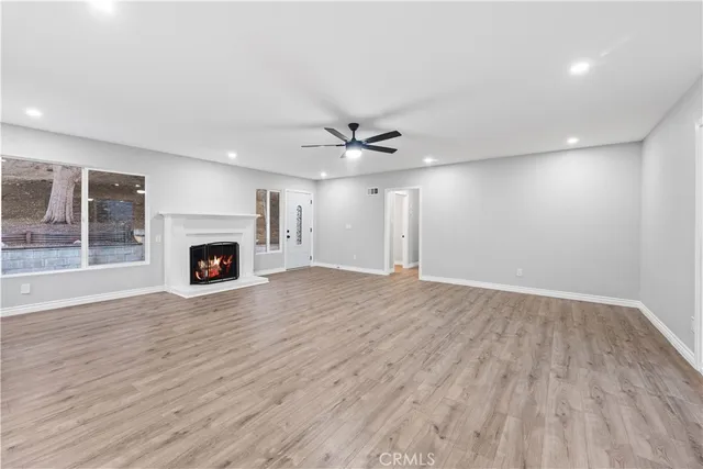 an empty room with wooden floor a ceiling fan a fireplace and windows