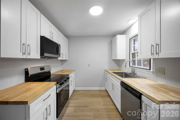 a kitchen with stainless steel appliances a sink dishwasher a stove top oven a refrigerator with grey cabinets and wooden floor