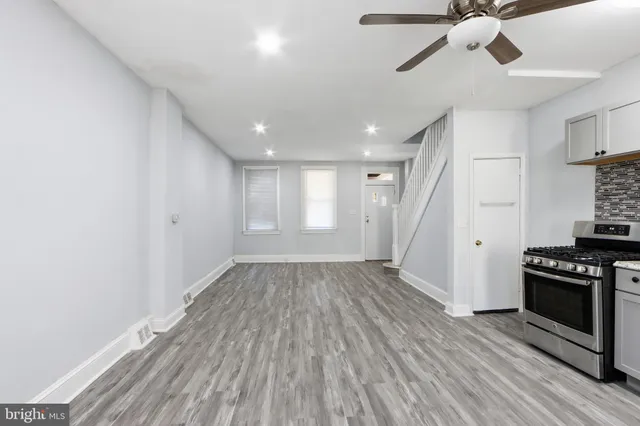 a view of an empty room with wooden floor fridge and a window