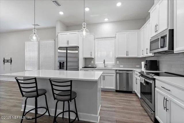 a kitchen with stainless steel appliances granite countertop a stove a sink dishwasher a refrigerator with white cabinets and wooden floor