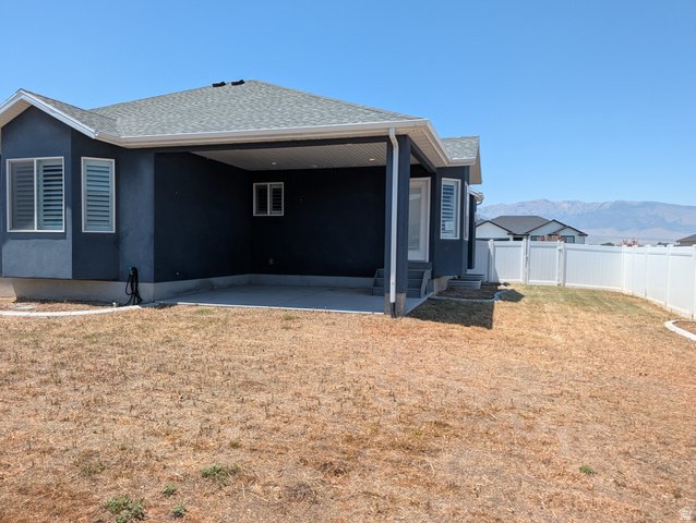171 South Mustang Road East Grantsville, UT 84029 - Photo 40 of 41 Backyard featuring a covered patio with concrete flooring, a white vinyl fence, and a distant mountain range backdrop