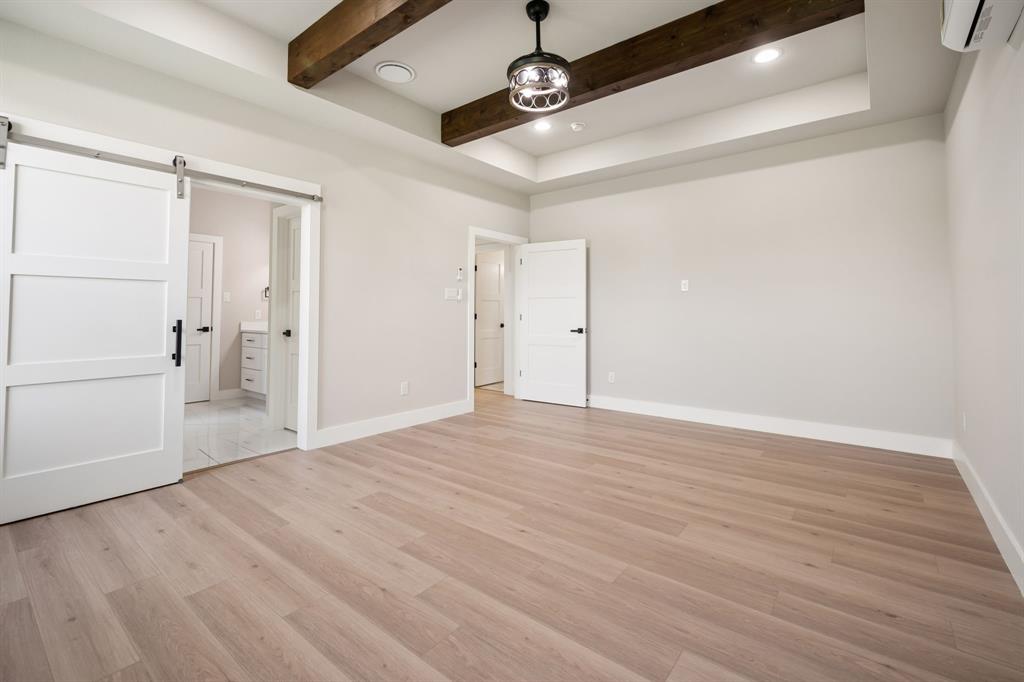 105 Buckboard Trail Oak Point, TX 75068 - Photo 13 of 27 First floor primary bedroom with barn door entry to bath, recessed lighting, ensuite bathroom, light wood finished floors, and beam ceiling
