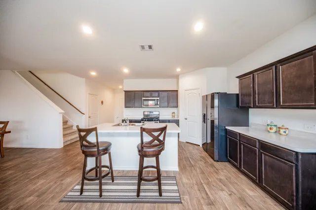 a kitchen with stainless steel appliances a refrigerator a stove top oven a sink dishwasher and white cabinets with wooden floor