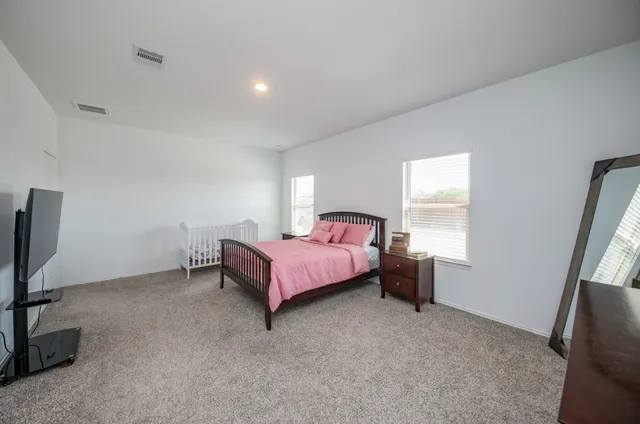 a spacious bedroom with a bed and a flat tv screen on the dresser