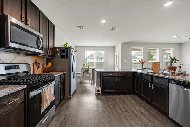 a kitchen with stainless steel appliances kitchen island granite countertop a stove a sink dishwasher and a microwave oven with wooden floor