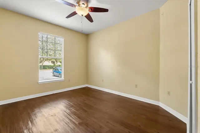 a view of an empty room with wooden floor and a ceiling fan