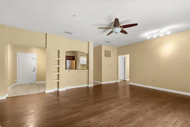 a view of an empty room with wooden floor and a ceiling fan