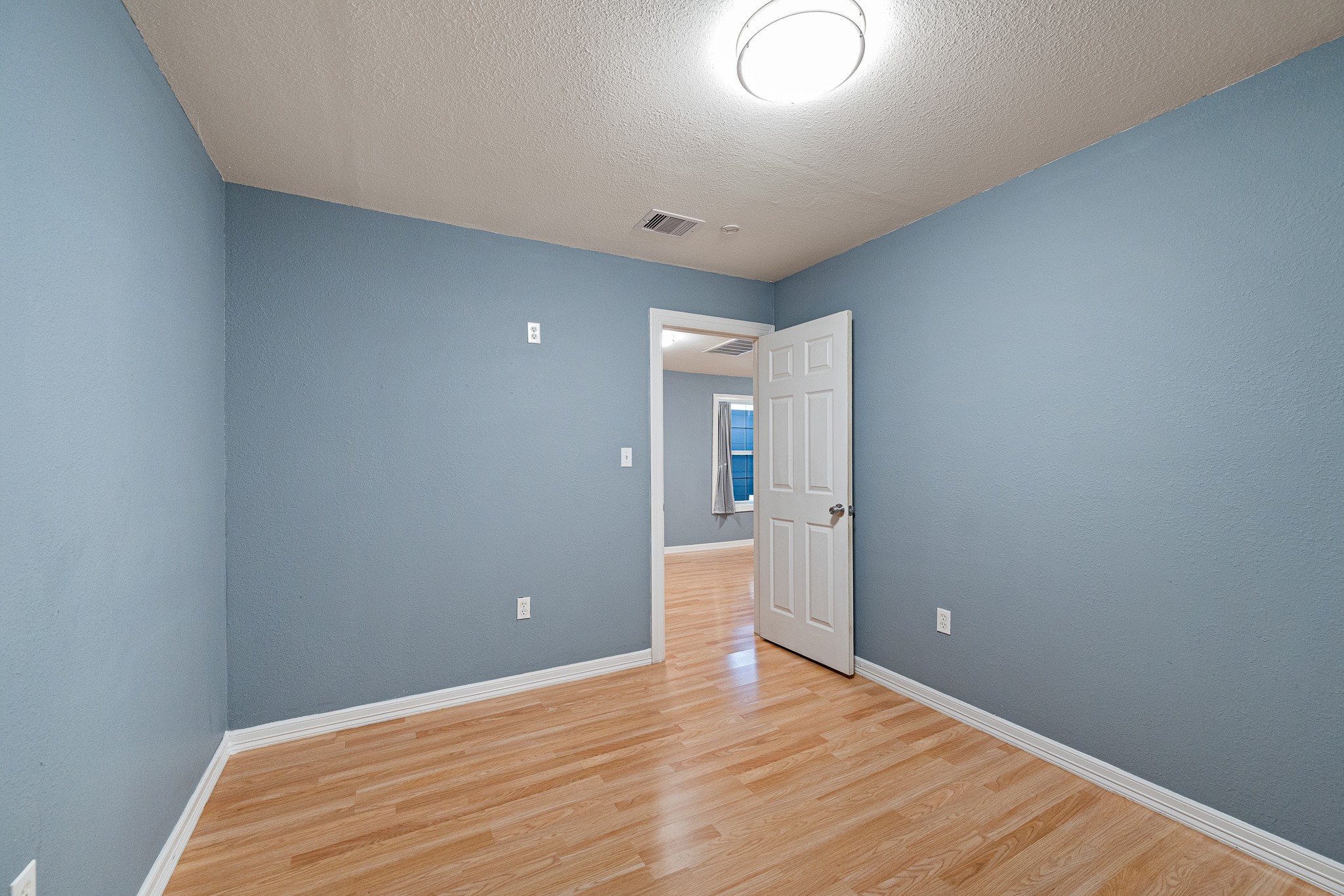 7815 Harding Street, Unit B Houston, TX 77012 - Photo 20 of 21 This inviting 2nd bedroom features soothing blue walls, warm flooring, and ample natural light, offering a cozy and serene retreat.