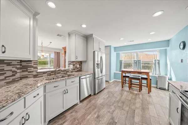 a kitchen with stainless steel appliances granite countertop a stove a sink dishwasher and a refrigerator with wooden floor