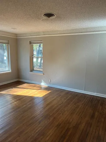 an empty room with wooden floor and windows with curtains