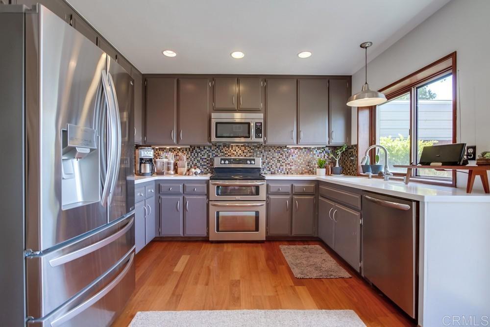 428 Compass Road Oceanside, CA 92054 - Photo 7 of 13 a kitchen with wooden floors white cabinets and stainless steel appliances