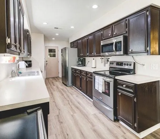 a kitchen with stainless steel appliances granite countertop a sink a stove top oven a refrigerator with grey cabinets