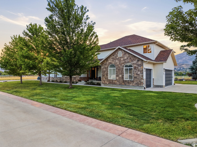 702 Alpine Highway Alpine, UT 84004 - Photo 6 of 83 Stone and stucco exterior with an attached garage, featuring a concrete driveway and mature trees bordering a manicured lawn