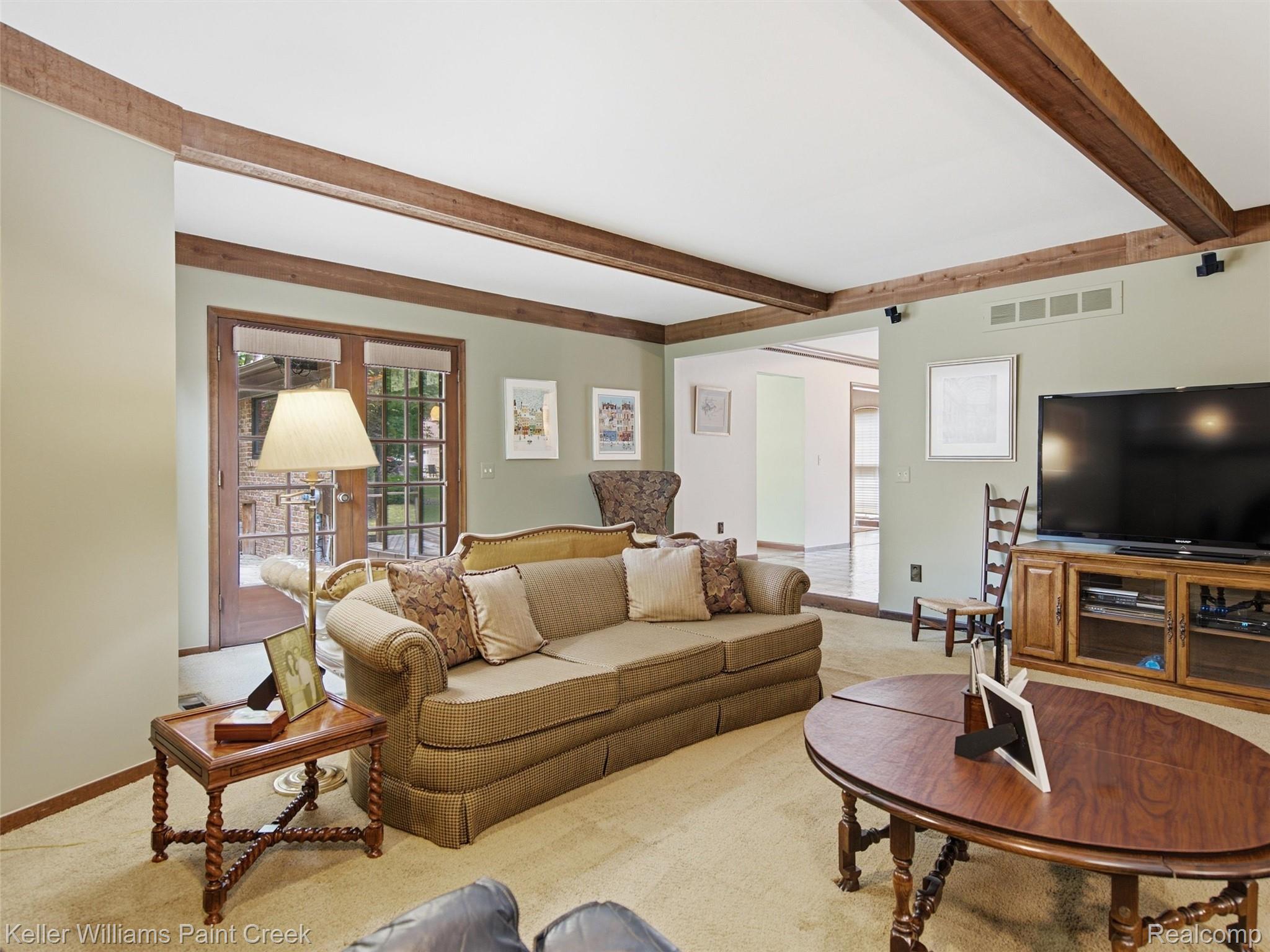 2950 Leyton Court Rochester, MI 48306 - Photo 15 of 46 Carpeted living space with exposed wood ceiling beams, light green wall paint, and a double glass-panel door