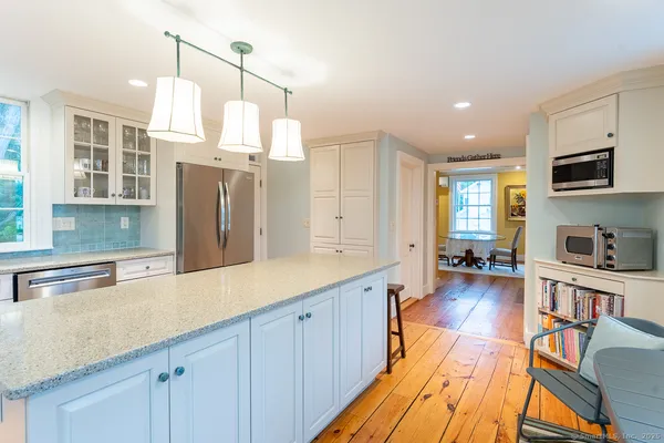 a kitchen with stainless steel appliances granite countertop a refrigerator a sink dishwasher a dining table and chairs with wooden floor