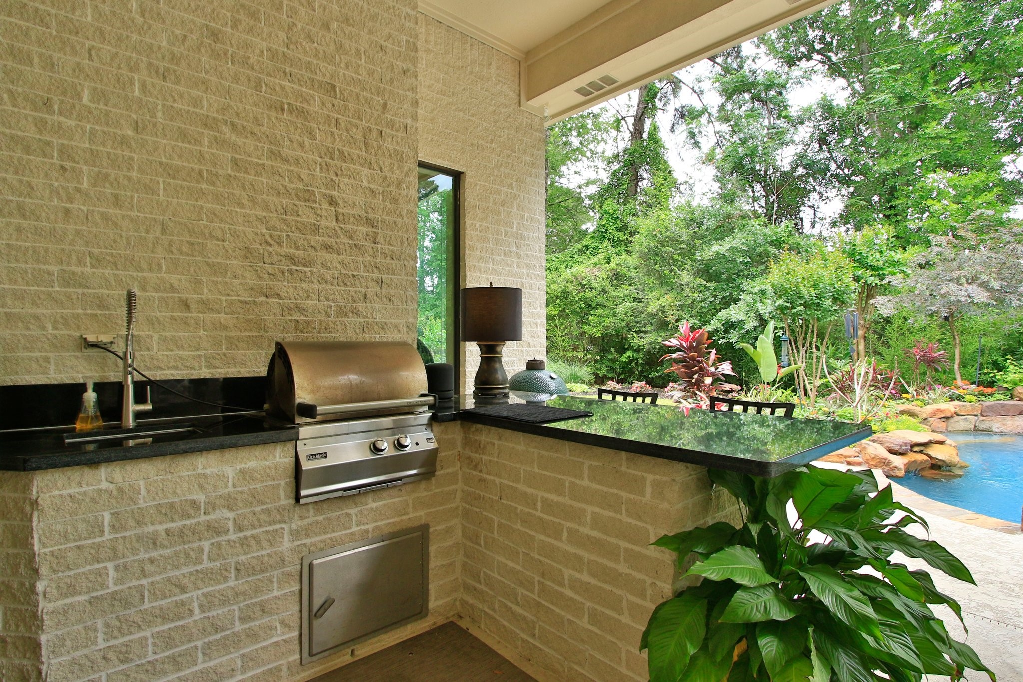 17511 Seidel Road Tomball, TX 77377 - Photo 9 of 49 This outdoor space features a built-in grill and sink with a sleek black countertop, perfect place for entertaining. It overlooks a lush garden and a sparkling pool, creating a serene and inviting atmosphere.