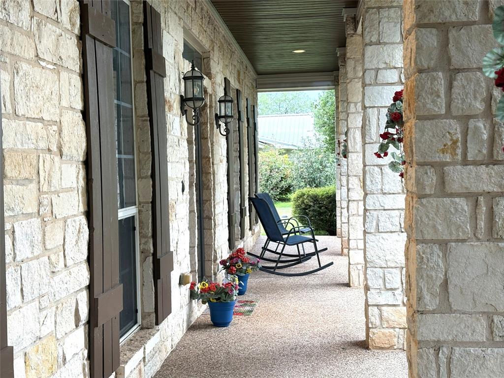 1170 Brazos Loop Gholson, TX 76705 - Photo 8 of 37 Covered stone-clad porch featuring decorative wall sconces, dark wood-finish shutters, and a textured aggregate flooring