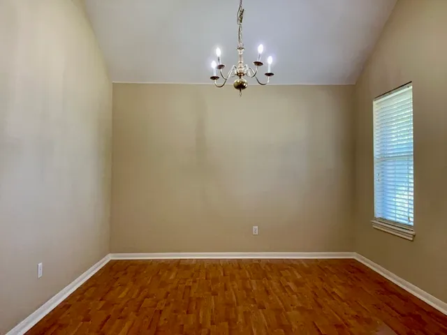 a view of an empty room with chandelier fan and wooden floor