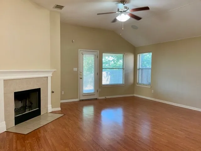 a view of an empty room with wooden floor fireplace and a window
