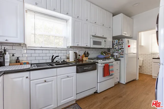 a kitchen with stainless steel appliances granite countertop white cabinets a sink a window and a refrigerator