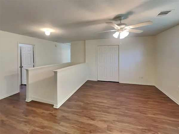a view of an empty room with wooden floor and a ceiling fan